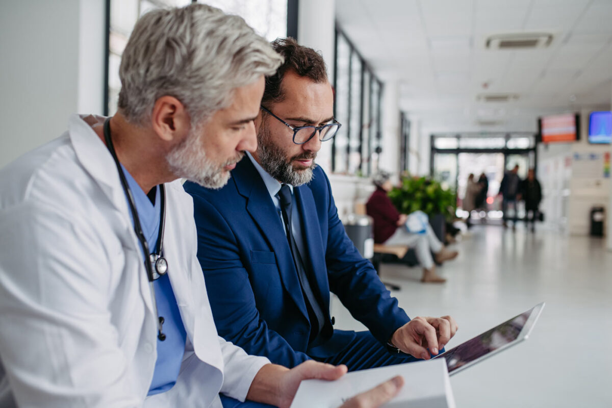 pharmaceutical sales representative talking with doctor in medical building, presenting new medication on tablet