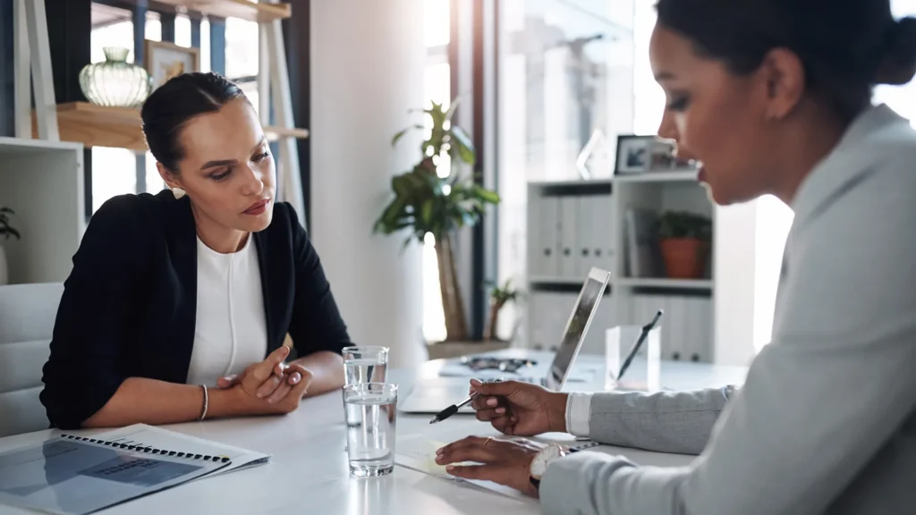 Two professionals review a candidate’s documents during an interview at an office desk.